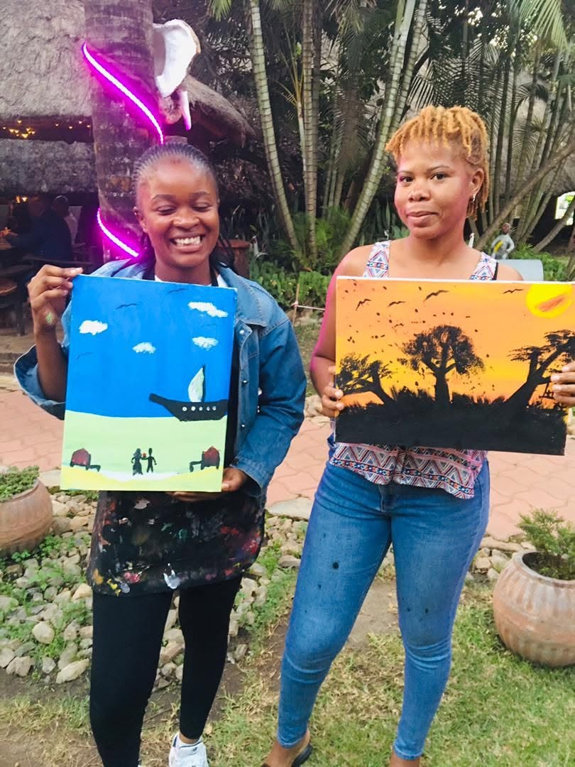Two guests smiling and holding their finished paintings